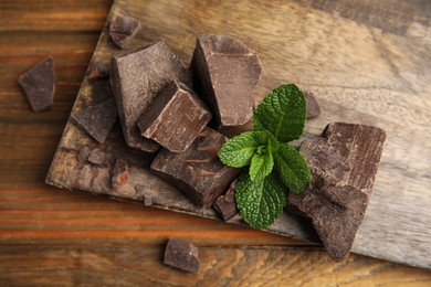 Tasty dark chocolate pieces with mint on wooden table, flat lay