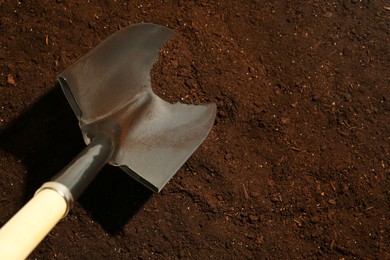 Photo of Metal shovel on fertile soil, space for text. Gardening tool