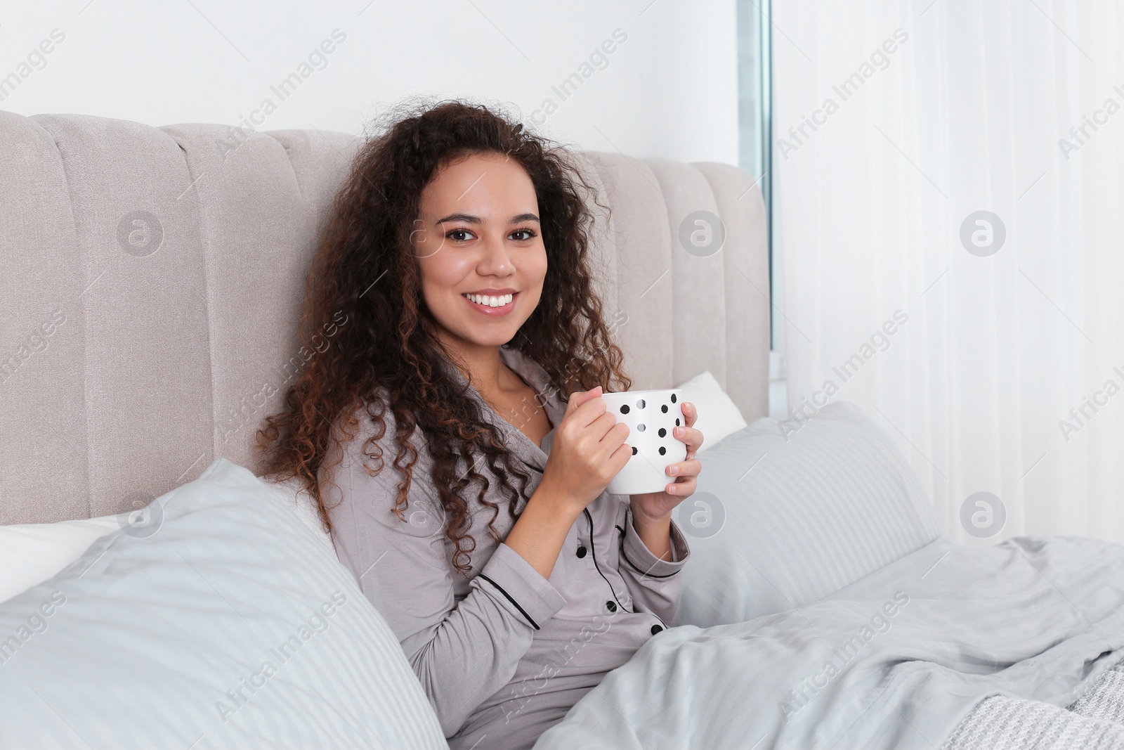 Photo of Beautiful African American woman with cup of drink in bed at home