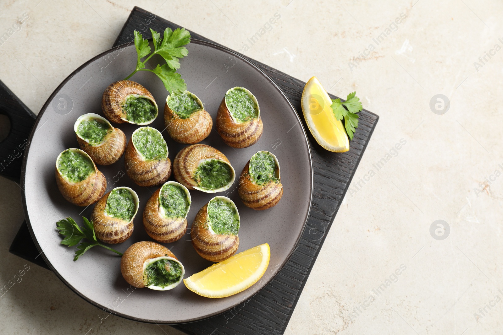Photo of Delicious cooked snails with parsley and lemon on light table, top view. Space for text
