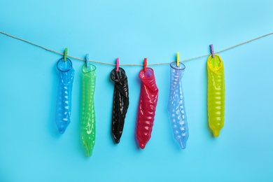 Used colorful condoms hanging on clothesline against light blue background. Safe sex concept