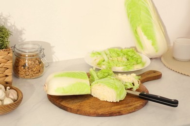 Photo of Cut fresh chinese cabbage and knife on white kitchen table