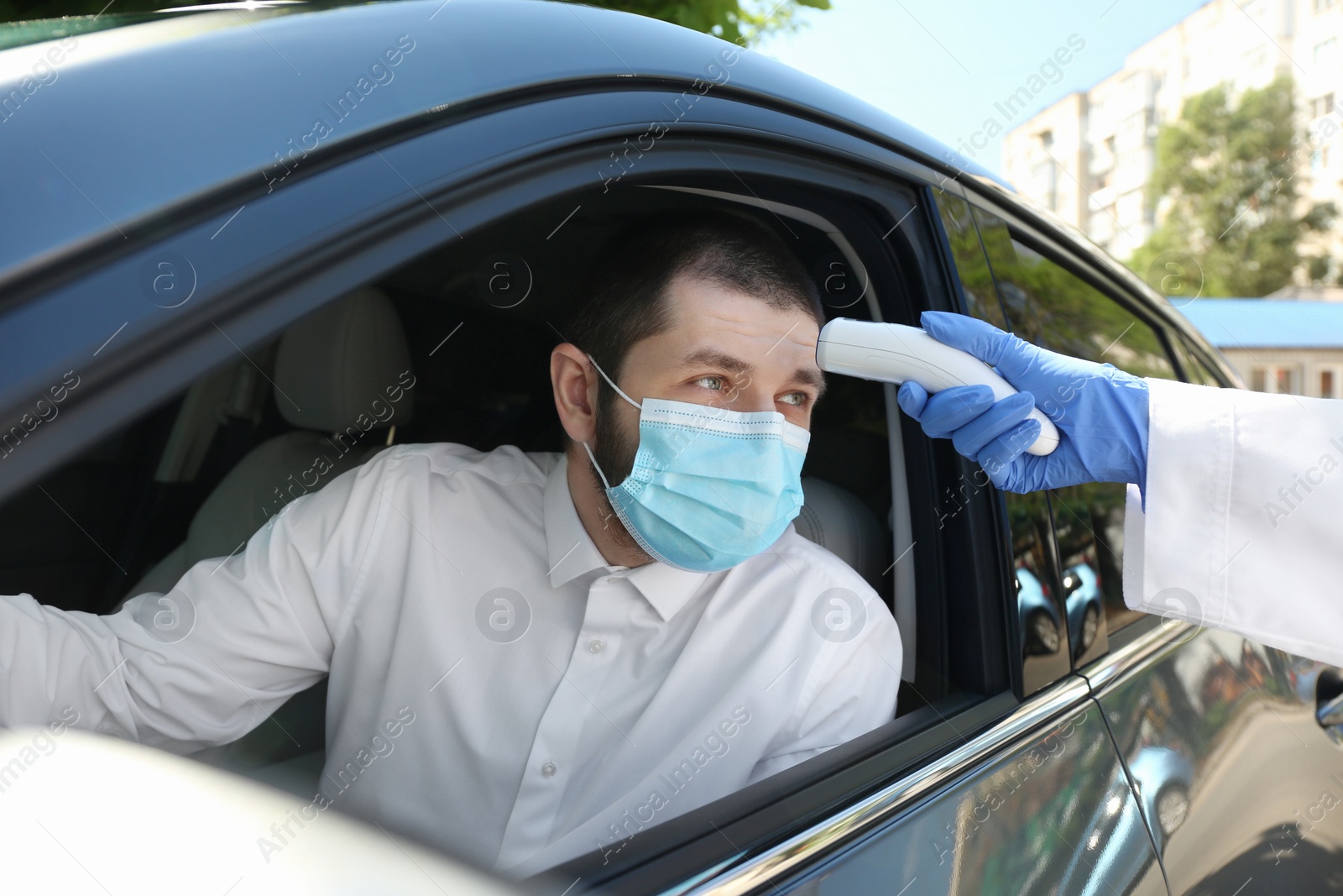 Photo of Doctor measuring driver's temperature with non contact infrared thermometer outdoors