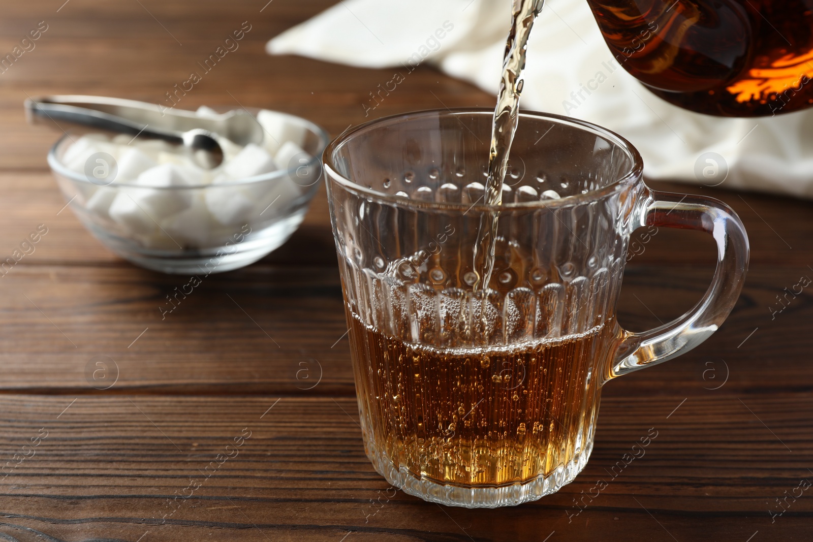 Photo of Pouring tea into glass cup at wooden table, closeup