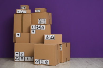 Photo of Cardboard boxes with different packaging symbols on floor near purple wall, space for text. Parcel delivery