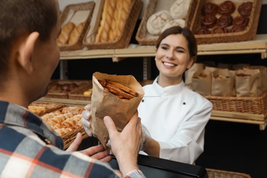 Baker giving customer paper bag with pastry in store