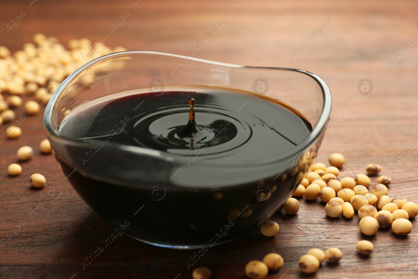 Photo of Soy sauce drops falling into bowl on wooden table, closeup