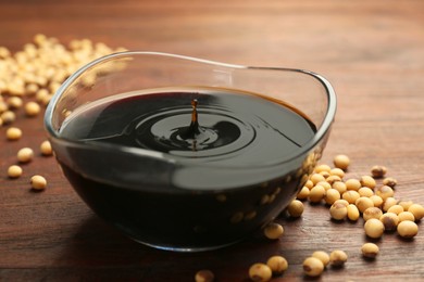 Photo of Soy sauce drops falling into bowl on wooden table, closeup