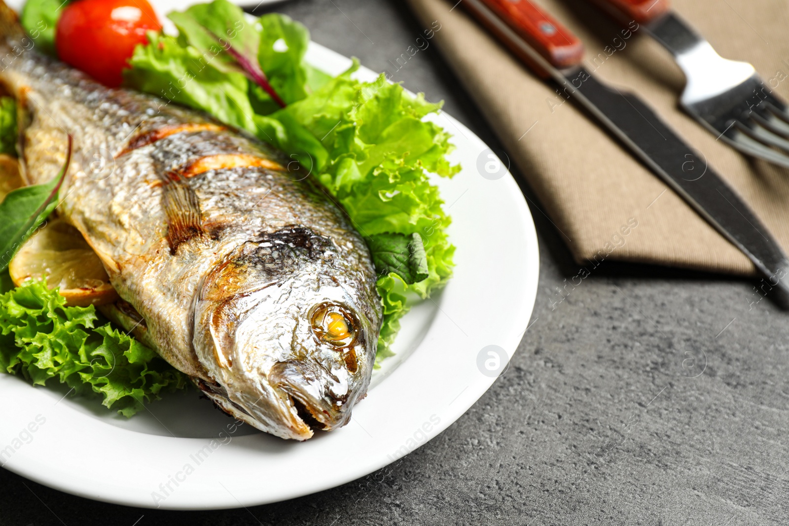 Photo of Delicious roasted fish with lemon and vegetables on dark grey background, closeup