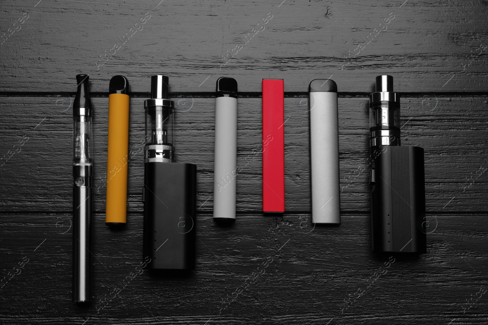 Photo of Group of different electronic cigarettes on black wooden table, flat lay. Smoking alternative