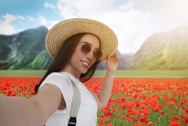 Image of Beautiful woman in straw hat with sunglasses taking selfie in poppy flowers near mountain