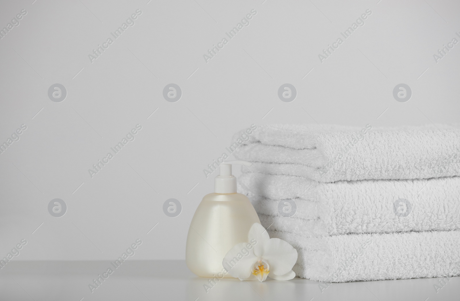 Photo of Soft folded towels, orchid flowers and dispenser on white table, space for text