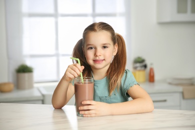 Photo of Cute little child with glass of tasty chocolate milk in kitchen