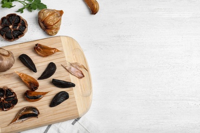 Photo of Flat lay composition with black garlic and space for text on white wooden table