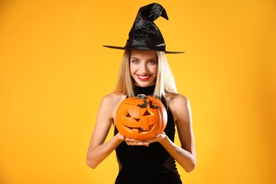 Photo of Beautiful woman in witch costume with jack o'lantern on yellow background. Halloween party