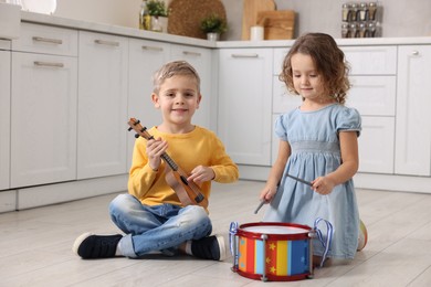 Little children playing toy musical instruments in kitchen