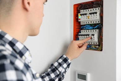 Young handyman pressing switch on electrical panel board indoors