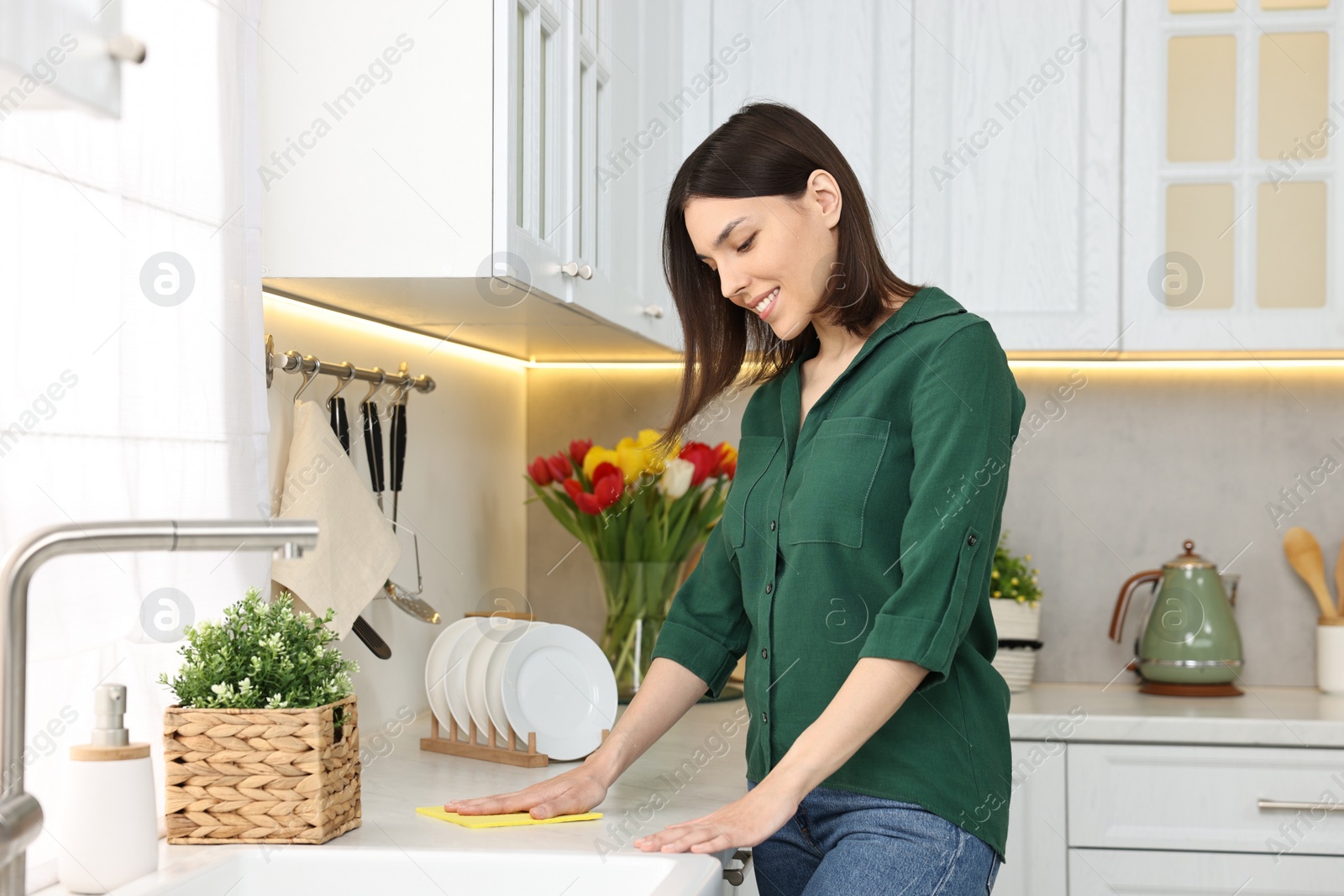 Photo of Woman cleaning furniture with sponge wipe in kitchen