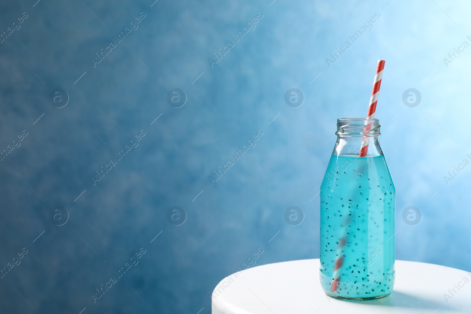 Photo of Light blue drink with basil seeds in bottle on white table, space for text