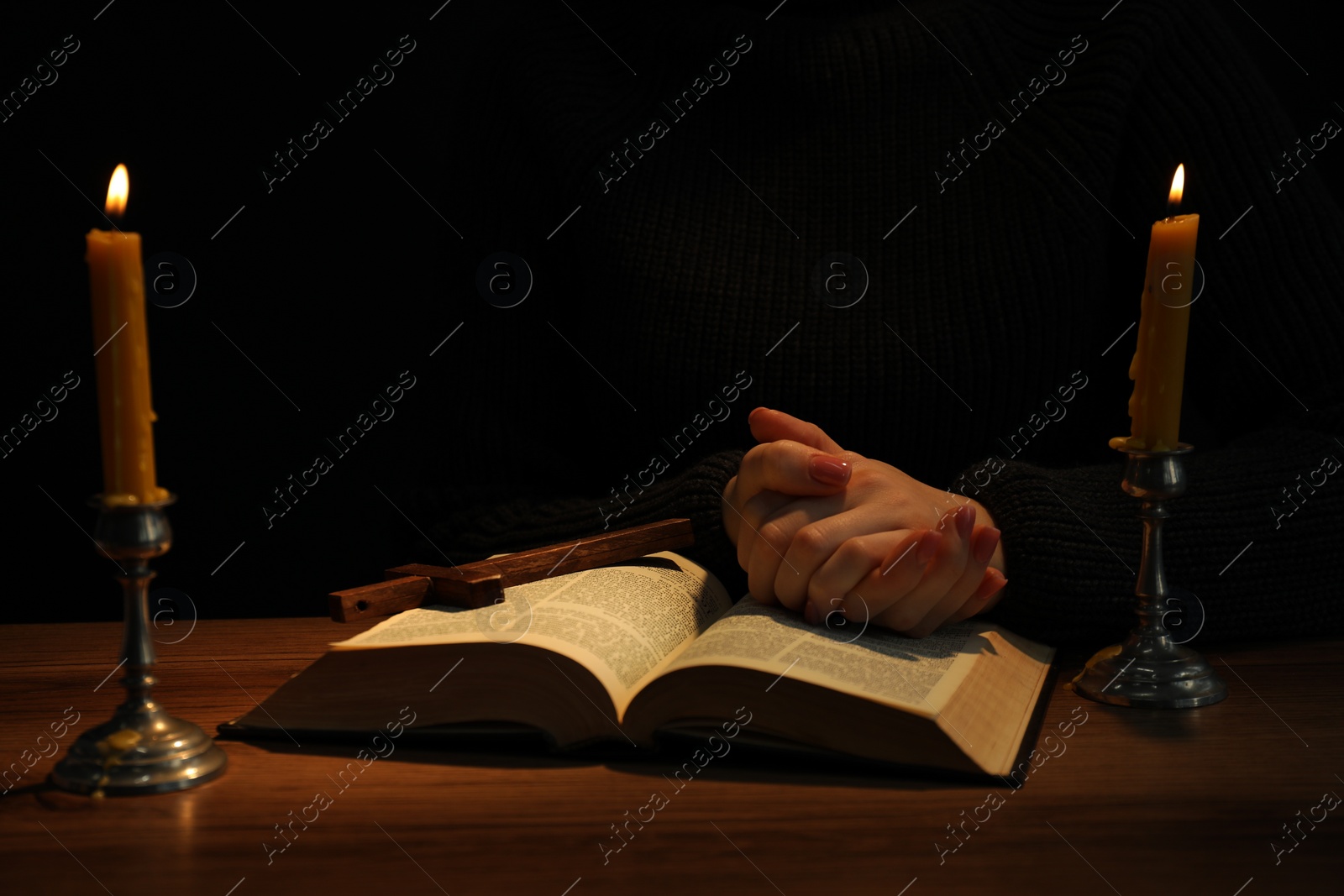 Photo of Woman praying at table with burning candles and Bible, closeup