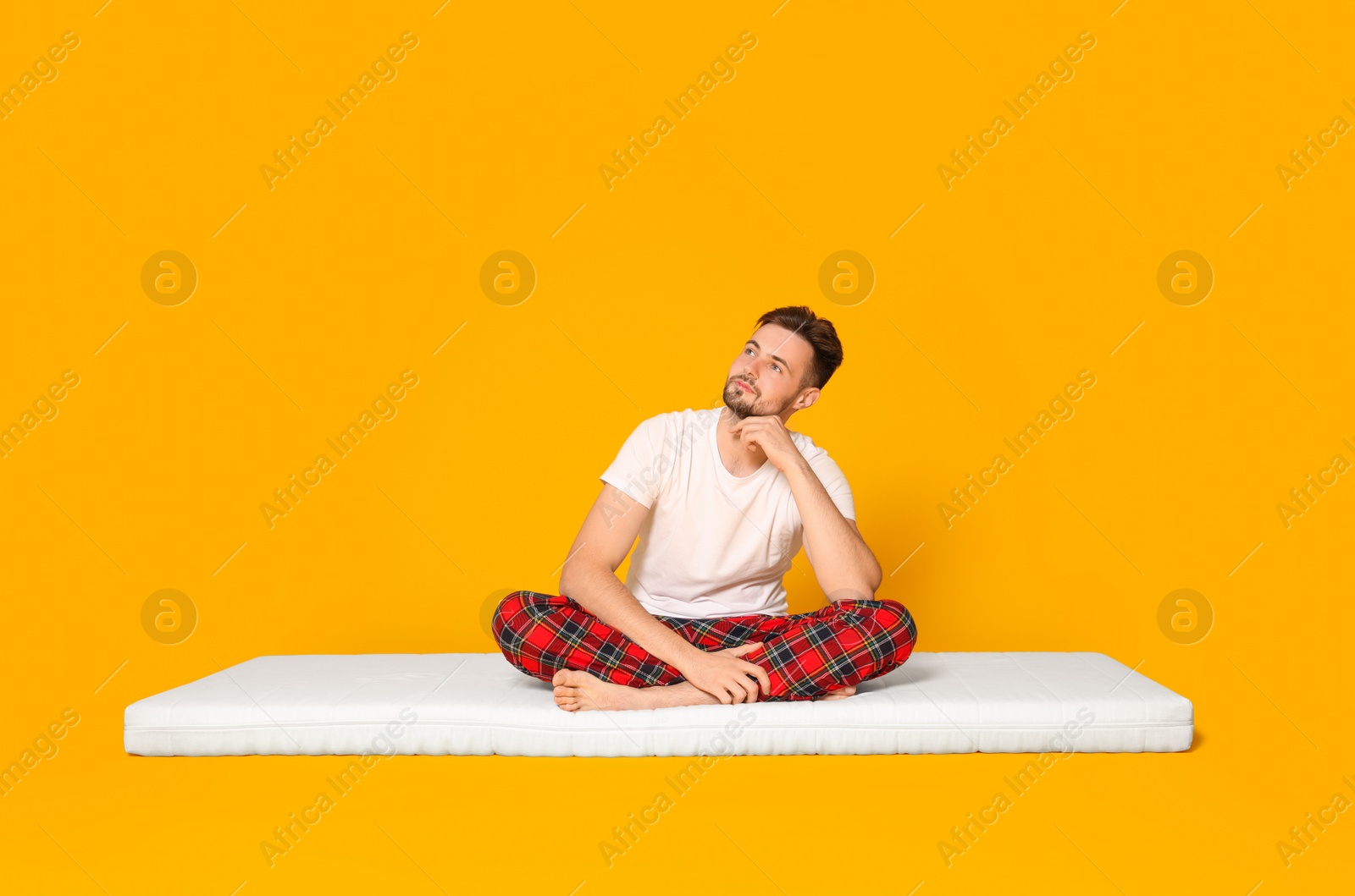 Photo of Man sitting on soft mattress against orange background