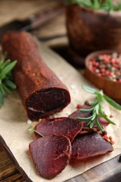 Photo of Delicious dry-cured beef basturma with rosemary and peppercorns on wooden table, closeup