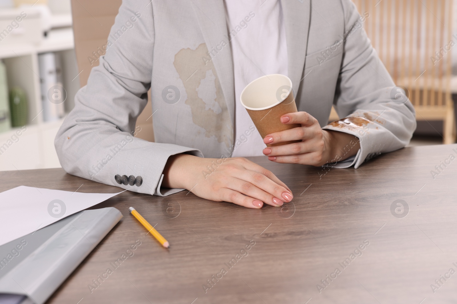 Photo of Woman showing stain from coffee on her jacket at wooden table indoors, closeup