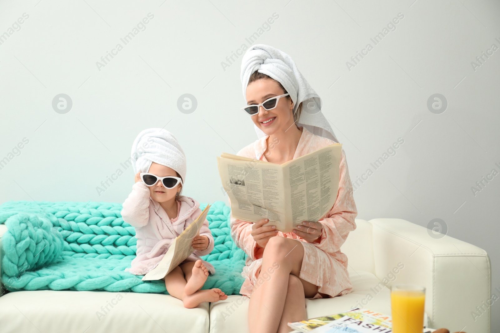 Photo of Mother and little daughter in bathrobes with newspapers sitting on sofa