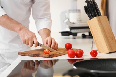 Photo of Professional chef cutting tomatoes in kitchen, closeup