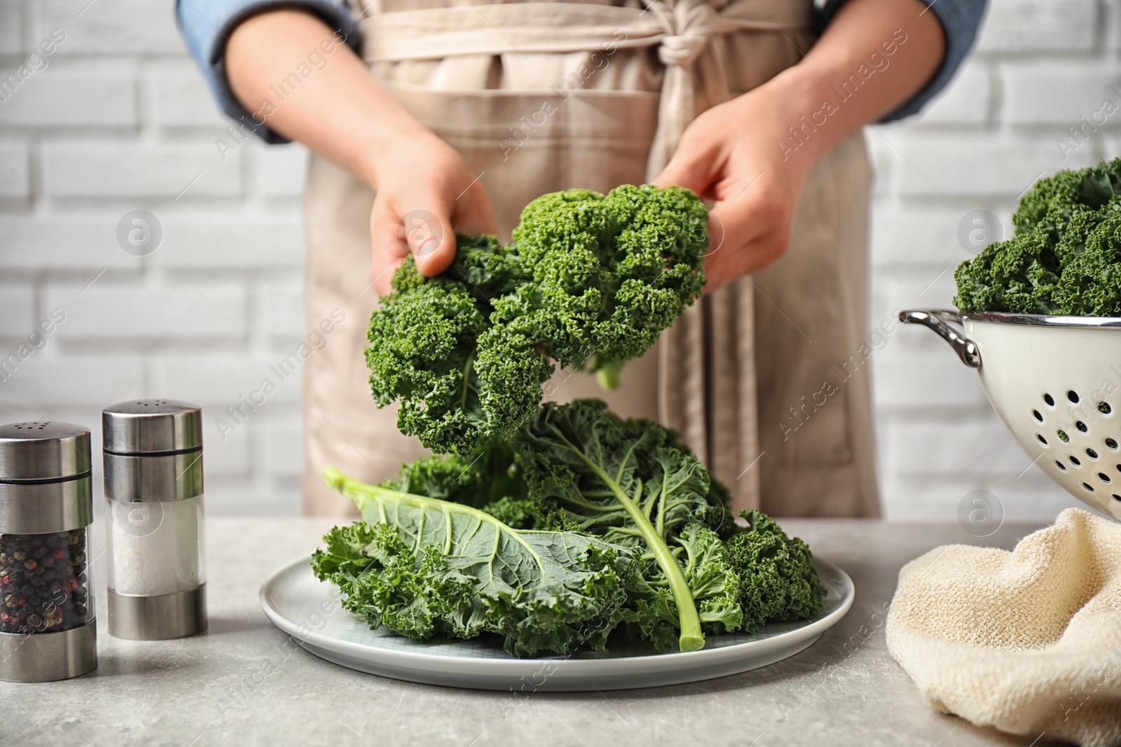 Photo of Woman holding fresh kale leaves over light grey table, closeup