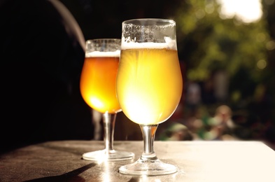 Photo of Glasses of cold tasty beer on wooden table outdoors