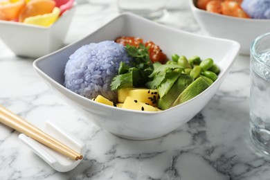 Photo of Poke bowl served on white marble table, closeup