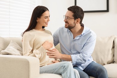 Photo of Happy pregnant woman spending time with her husband on sofa at home