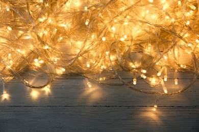 Photo of Glowing Christmas lights on white wooden background, top view