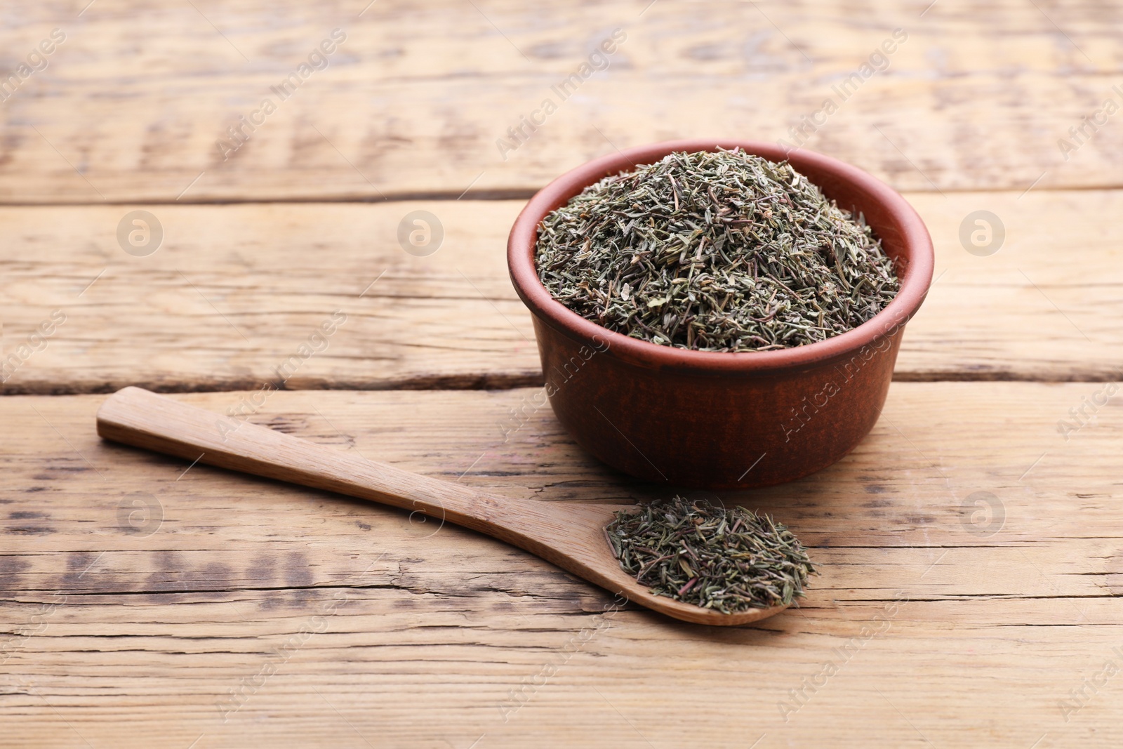 Photo of Bowl and spoon with dried thyme on wooden table