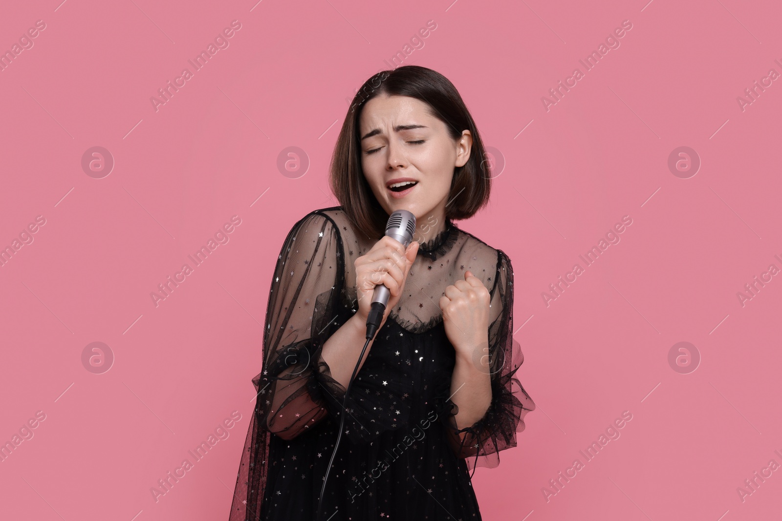 Photo of Beautiful young woman with microphone singing on pink background