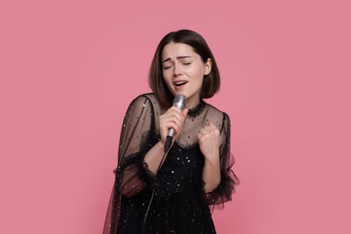 Beautiful young woman with microphone singing on pink background