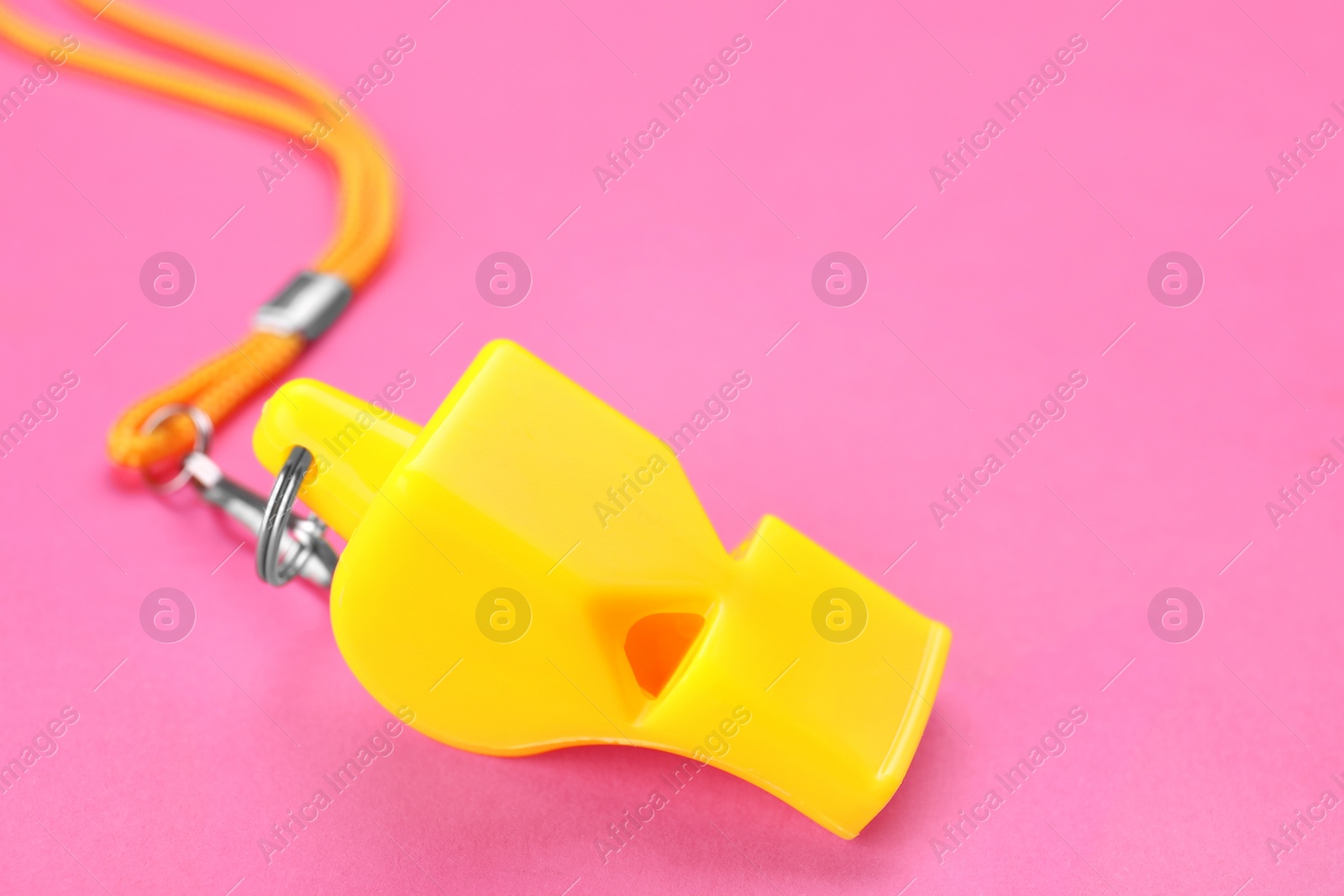 Photo of One yellow whistle with cord on pink background, closeup
