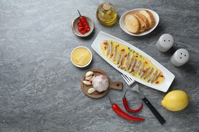 Photo of Tasty pickled anchovies with spices and products on gray table, flat lay. Space for text