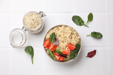 Photo of Tasty quinoa porridge with tomatoes and spinach in bowl on white tiled table, flat lay