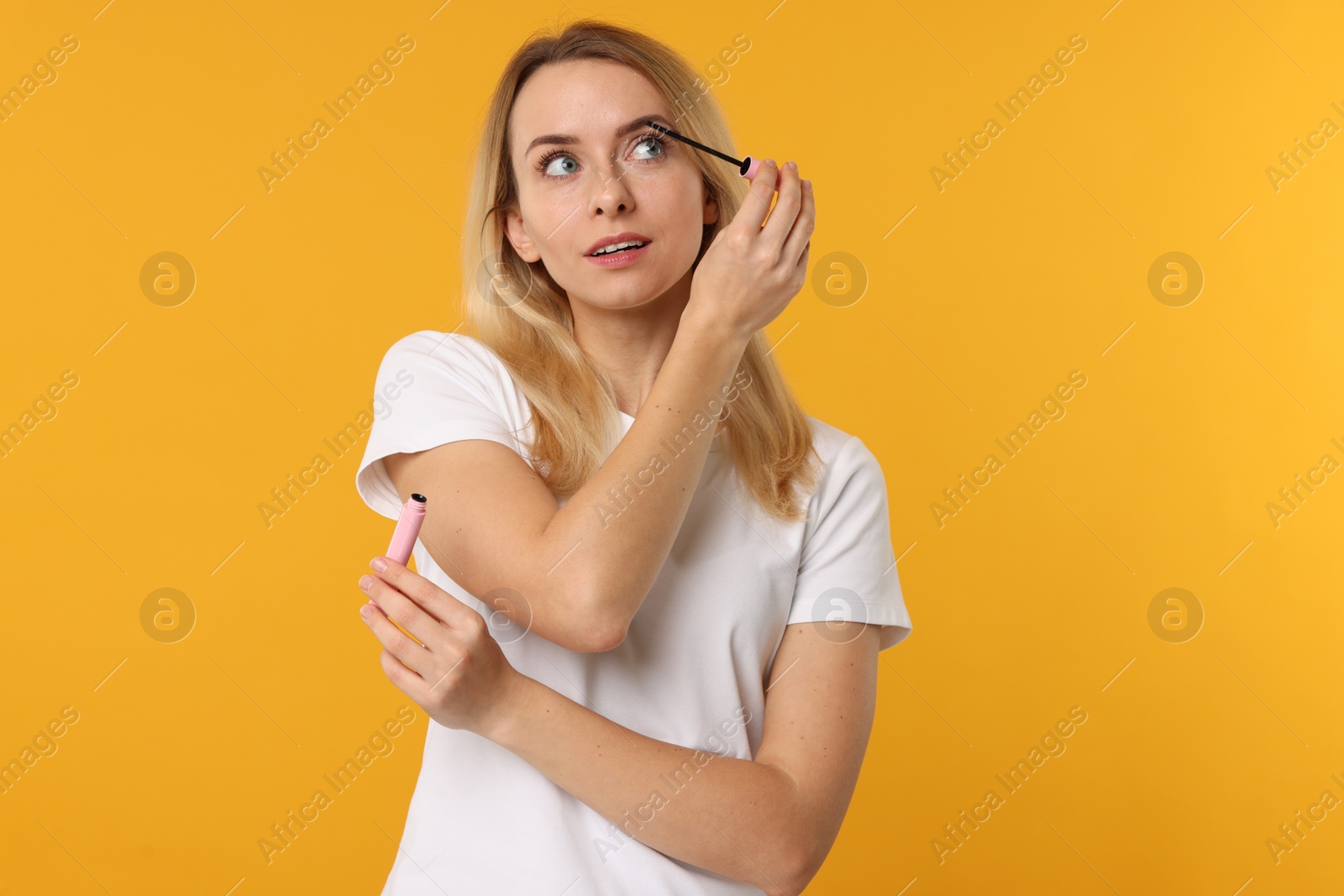 Photo of Beautiful woman applying mascara on orange background