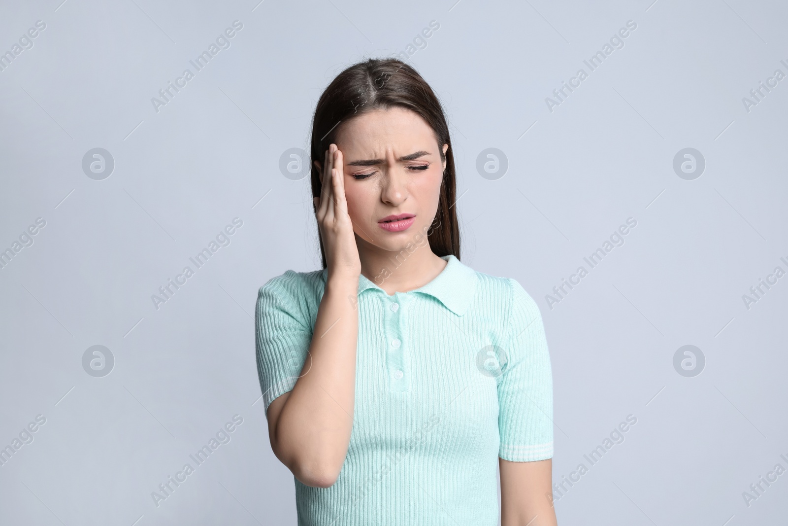 Photo of Young woman suffering from headache on light background