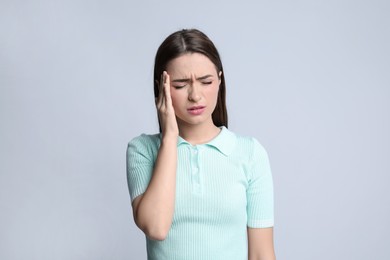 Young woman suffering from headache on light background