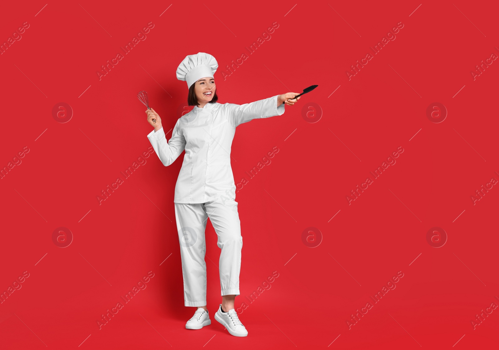 Photo of Happy confectioner holding whisk and spatula on red background