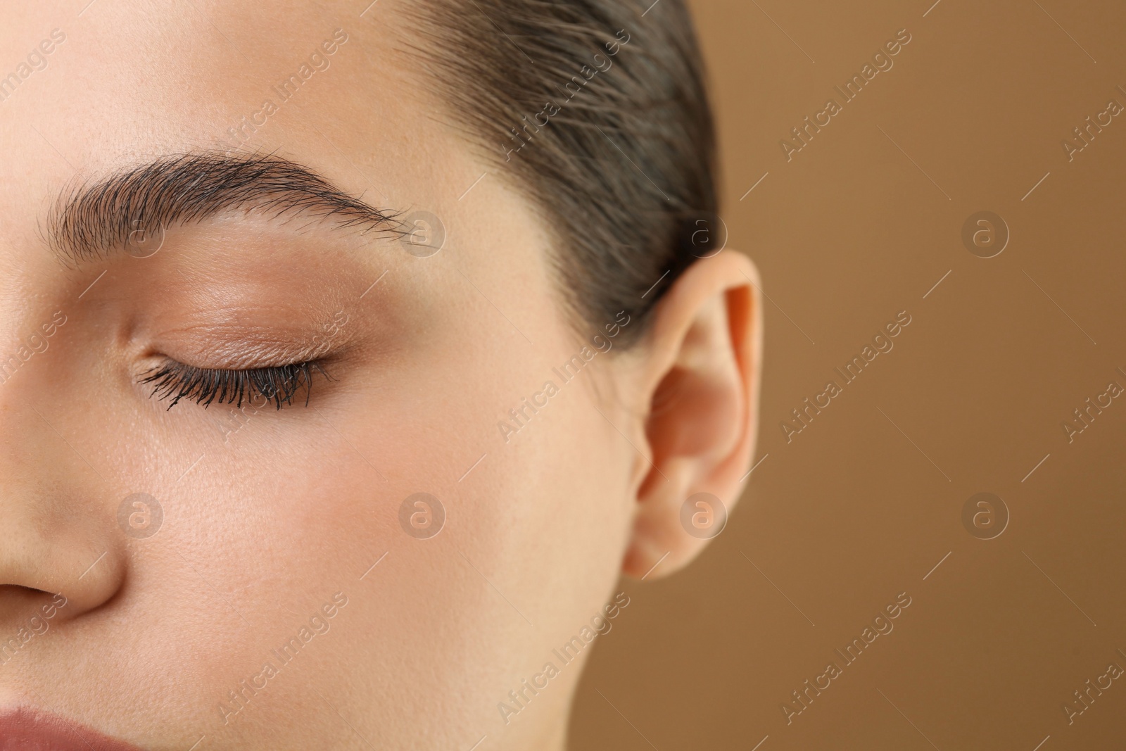 Photo of Young woman with perfect eyebrows on brown background, closeup. Space for text