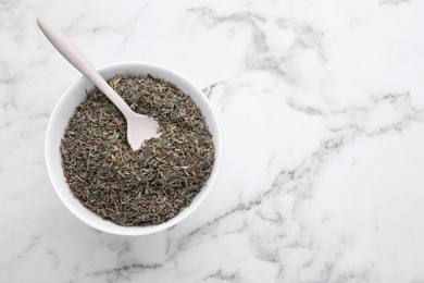 Photo of Bowl with dried thyme and spoon on white marble table, top view. Space for text