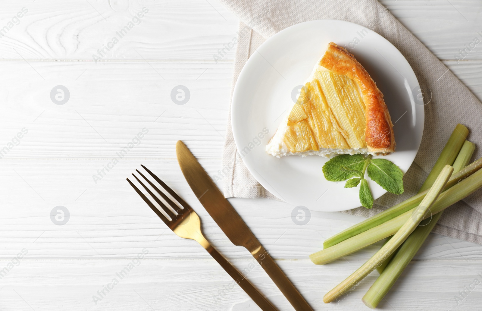 Photo of Piece of freshly baked rhubarb pie, stalks and cutlery on white wooden table, flat lay. Space for text