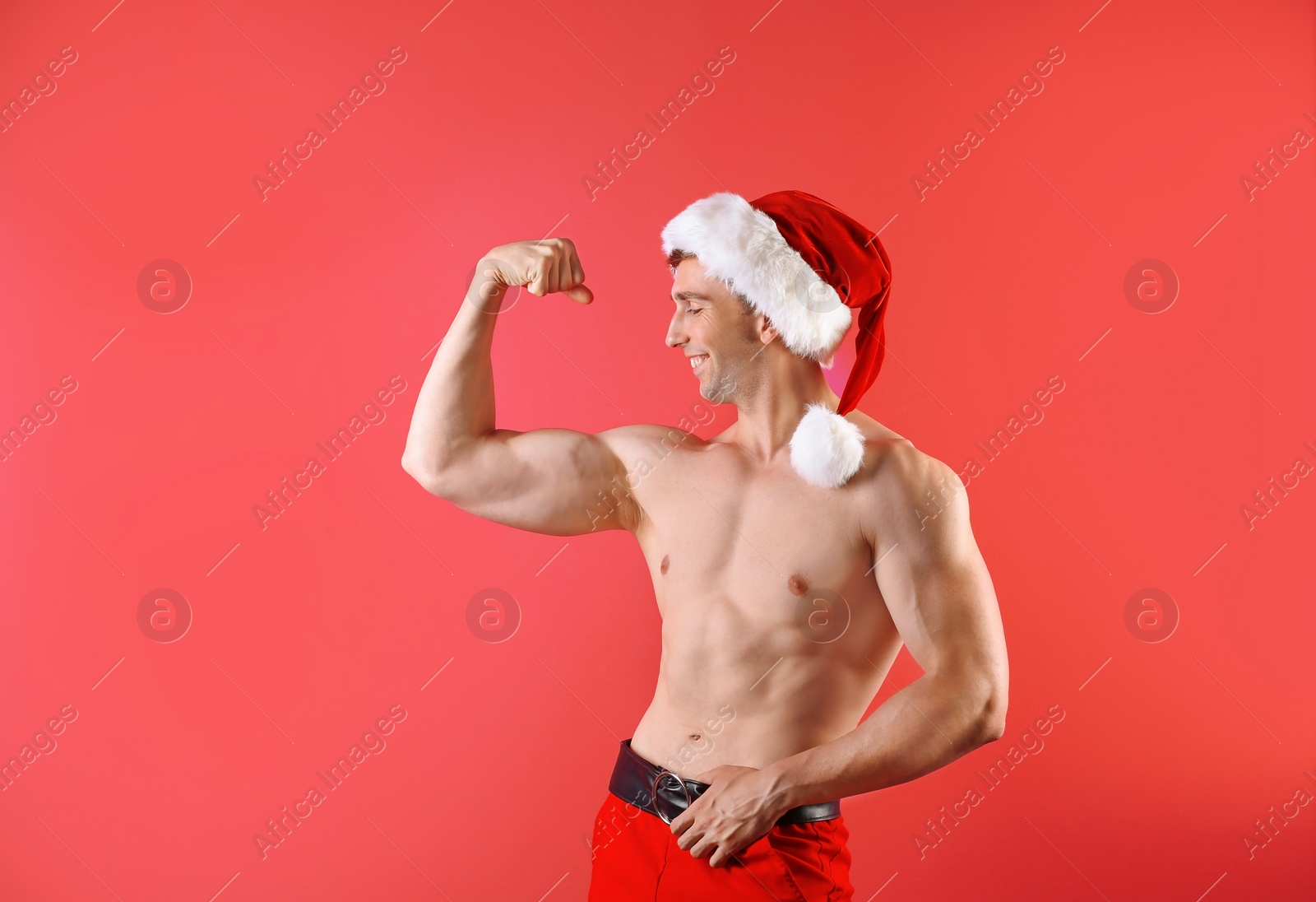 Photo of Young muscular man in Santa hat on color background