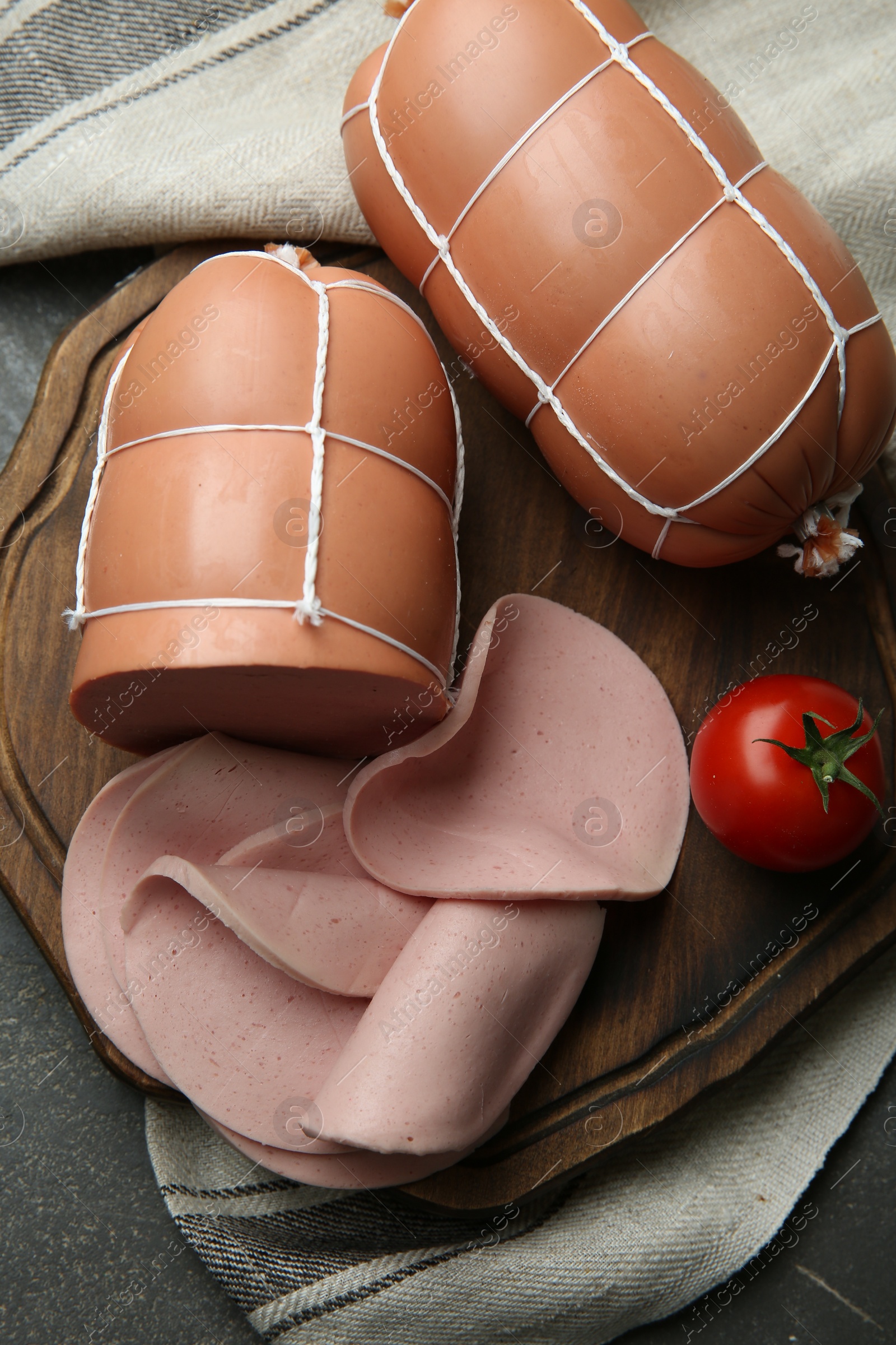 Photo of Board with tasty boiled sausages and tomato on grey textured table, flat lay