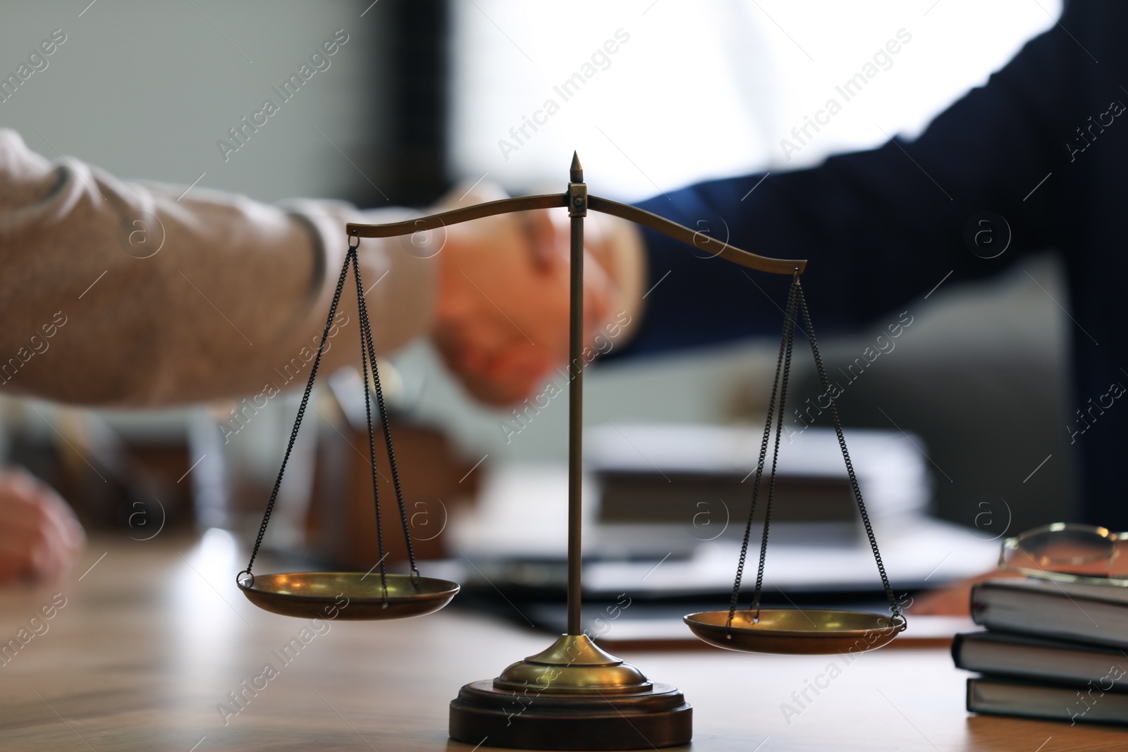 Photo of Male lawyer shaking hands with client in office, focus on scales of justice